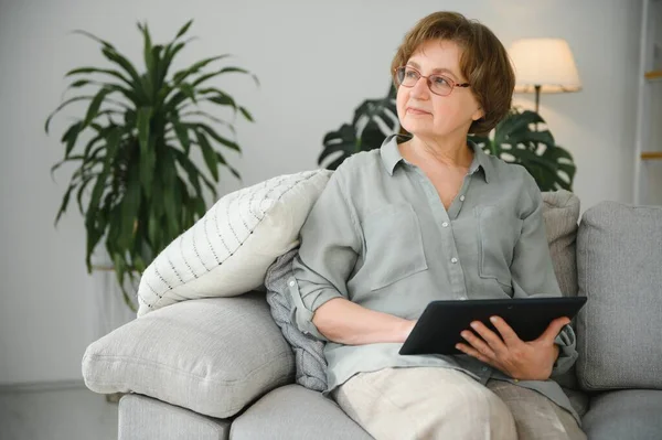 Yaşlı kadın evdeki oturma odasında dijital tablet kullanıyor..