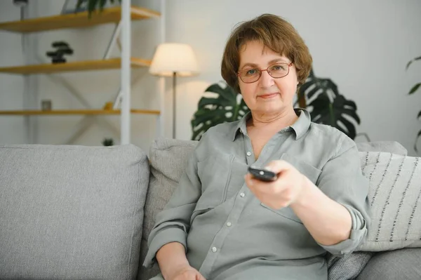 Yaşlı kadın İşitme işareti yapıyor, yükselen televizyon sesi uzaktan kumandayla ayarlanıyor