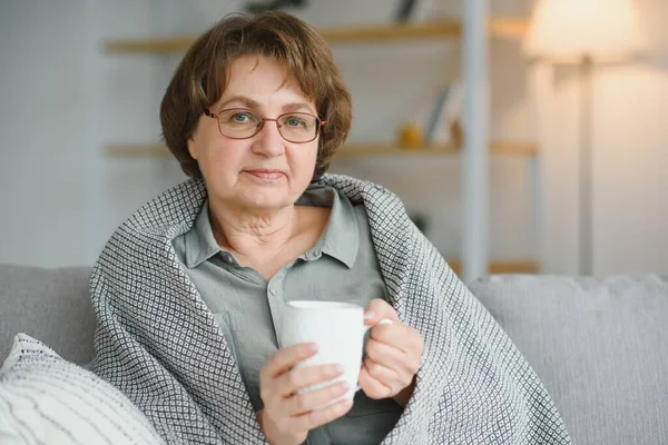老年的高加索养恤金领取者 裹着灰色格子布 在客厅里喝热茶 — 图库照片
