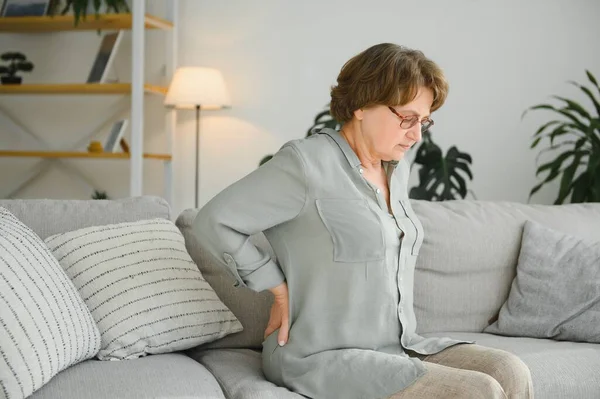 成熟的女士坐在床上摸她的背 神经根炎和疼痛 — 图库照片