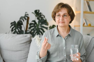 Yaşlı kadın kanepede oturuyor ve evde hap alıyor. İlaç kullanan emekliler..