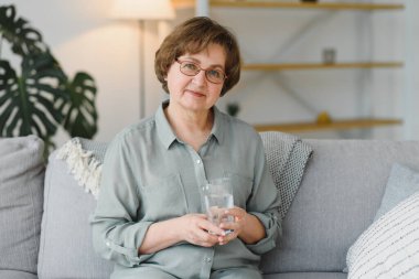 Yaşlı kadın kanepede oturuyor ve evde hap alıyor. İlaç kullanan emekliler..