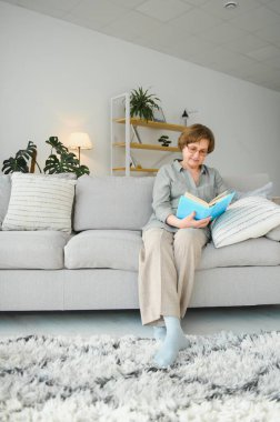 Çekici odaklı neşeli kadının portresi divanda oturmuş kitap okuyor. Ev içinde boş hayaller kuruyor.