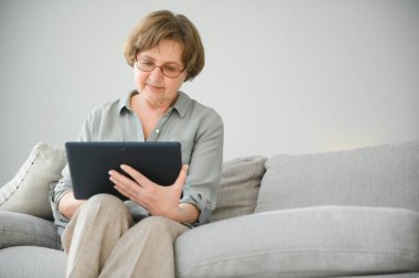 Kanepedeki dijital tabletine bakıp gülen son sınıf öğrencisi kadın..