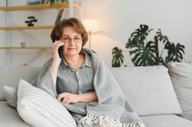 Mutlu gülümseyen Kafkasyalı yaşlı yaşlı kadın büyükannesi arkadaşlarıyla, torunlarıyla, iş arkadaşlarıyla cep telefonuyla, evdeki akıllı telefonuyla konuşuyor.