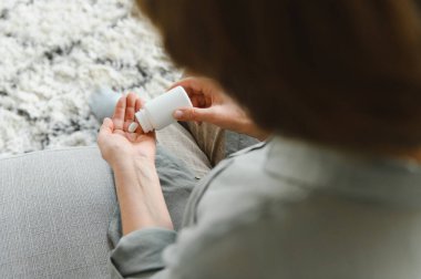 Yaşlı kadın kanepede oturuyor ve evde hap alıyor. İlaç kullanan emekliler..