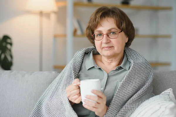 安逸悠闲的老年老太太奶奶在家里喝着热饮茶咖啡 看着客厅里的相机 养恤金概念 — 图库照片