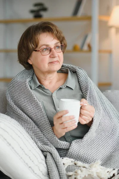 安逸悠闲的老年老太太奶奶在家里喝着热饮茶咖啡 看着客厅里的相机 养恤金概念 — 图库照片