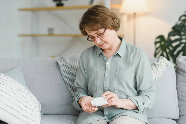 年长的女人坐在沙发上 在家里吃药 有药物的养恤金领取者 — 图库照片