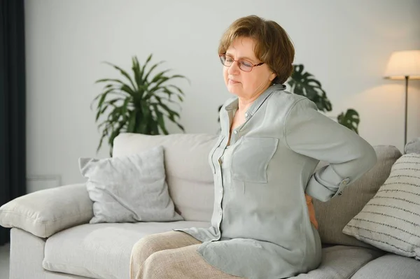 成熟的女士坐在床上摸她的背 神经根炎和疼痛 — 图库照片