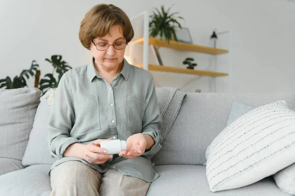 年长的女人坐在沙发上 在家里吃药 有药物的养恤金领取者 — 图库照片