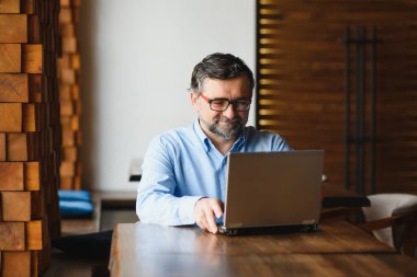 İş, teknoloji ve insan kavramı, dizüstü bilgisayarlı kıdemli işadamı modern kafede kahve içiyor.