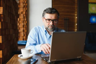 Kafede dizüstü bilgisayarda çalışan son sınıf erkek serbest yazar. uzak çalışma konsepti