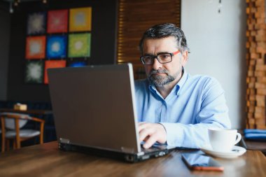 Kafede dizüstü bilgisayarda çalışan son sınıf erkek serbest yazar. uzak çalışma konsepti