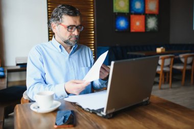 İş, teknoloji ve insan kavramı, dizüstü bilgisayarlı kıdemli işadamı modern kafede kahve içiyor.