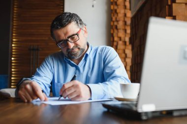 Kafede kahve içen olgun bir iş adamı. Güzel gözlükler takan, dizüstü bilgisayar kullanan, kameraya bakıp gülümseyen yakışıklı bir adamın portresi. Kahve molası.