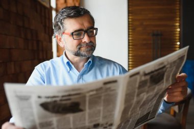 Gazete okuyan ve restoranda kahve içen aktif kıdemli bir adam..