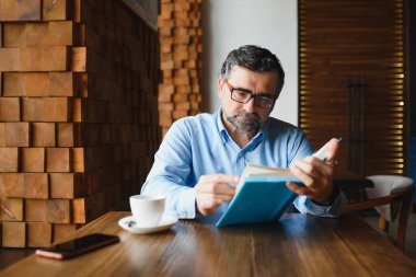 Kafede kitap okuyan olgun, yakışıklı bir adam..