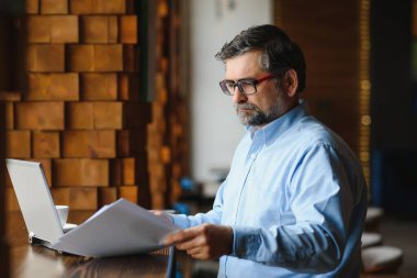 İş, teknoloji ve insan kavramı, dizüstü bilgisayarlı kıdemli işadamı modern kafede kahve içiyor.