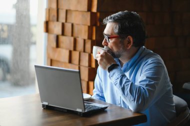 Kafede kahve içen olgun bir iş adamı. Güzel gözlükler takan, dizüstü bilgisayar kullanan, kameraya bakıp gülümseyen yakışıklı bir adamın portresi. Kahve molası.