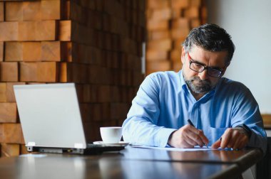İş, teknoloji ve insan kavramı, dizüstü bilgisayarlı kıdemli işadamı modern kafede kahve içiyor.