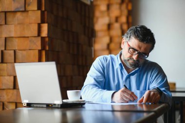İş, teknoloji ve insan kavramı, dizüstü bilgisayarlı kıdemli işadamı modern kafede kahve içiyor.