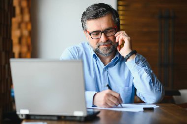 İş, teknoloji ve insan kavramı, dizüstü bilgisayarlı kıdemli işadamı modern kafede kahve içiyor.