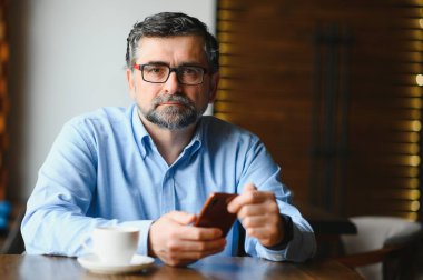 Restoranda oturup öğle yemeğini bekleyen mutlu iş adamı. Akıllı telefon kullanıyor ve biriyle konuşuyor. İş dünyası yaşlıları yaşam tarzı konsepti