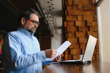 Erkek serbest yazar yeni bir iş projesi için bir kafede çalışıyor. Masadaki büyük bir pencerede oturuyor. Bir fincan kahveyle dizüstü bilgisayara bakıyor..