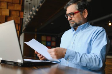 Kafede kahve içen olgun bir iş adamı. Güzel gözlükler takan, dizüstü bilgisayar kullanan, kameraya bakıp gülümseyen yakışıklı bir adamın portresi. Kahve molası.