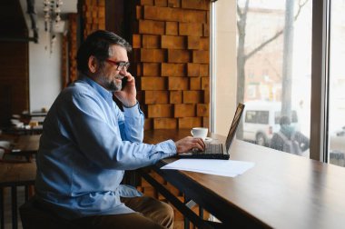 Restoranda oturup öğle yemeğini bekleyen mutlu iş adamı. Akıllı telefon kullanıyor ve biriyle konuşuyor. İş dünyası yaşlıları yaşam tarzı konsepti