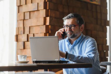 Kafede kahve içen olgun bir iş adamı. Güzel gözlükler takan, dizüstü bilgisayar kullanan, kameraya bakıp gülümseyen yakışıklı bir adamın portresi. Kahve molası.