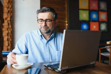 Kafede kahve içen olgun bir iş adamı. Güzel gözlükler takan, dizüstü bilgisayar kullanan, kameraya bakıp gülümseyen yakışıklı bir adamın portresi. Kahve molası.