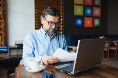 İş, teknoloji ve insan kavramı, dizüstü bilgisayarlı kıdemli işadamı modern kafede kahve içiyor.