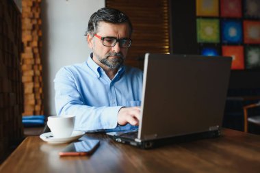 Kafede kahve içen olgun bir iş adamı. Güzel gözlükler takan, dizüstü bilgisayar kullanan, kameraya bakıp gülümseyen yakışıklı bir adamın portresi. Kahve molası.