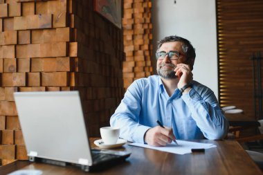 Kafede kahve içen olgun bir iş adamı. Güzel gözlükler takan, dizüstü bilgisayar kullanan, kameraya bakıp gülümseyen yakışıklı bir adamın portresi. Kahve molası.