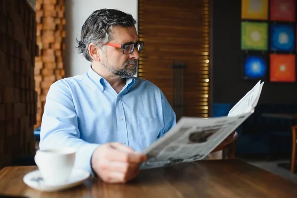 active senior man reading newspaper and drinking coffee in restaurant.