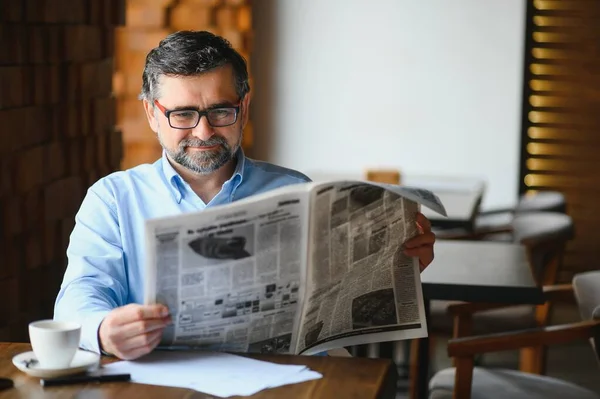 active senior man reading newspaper and drinking coffee in restaurant.