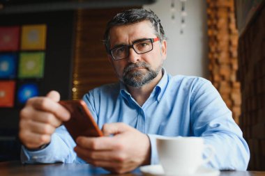 Restoranda oturup öğle yemeğini bekleyen mutlu iş adamı. Akıllı telefon kullanıyor ve biriyle konuşuyor. İş dünyası yaşlıları yaşam tarzı konsepti
