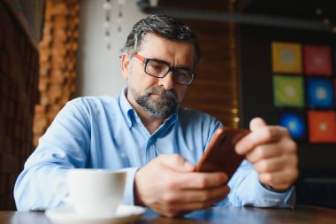 Restoranda oturup öğle yemeğini bekleyen mutlu iş adamı. Akıllı telefon kullanıyor ve biriyle konuşuyor. İş dünyası yaşlıları yaşam tarzı konsepti