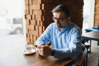 Restoranda oturup öğle yemeğini bekleyen mutlu iş adamı. Akıllı telefon kullanıyor ve biriyle konuşuyor. İş dünyası yaşlıları yaşam tarzı konsepti
