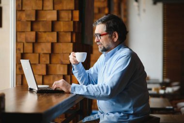 Kafede kahve içen olgun bir iş adamı. Güzel gözlükler takan, dizüstü bilgisayar kullanan, kameraya bakıp gülümseyen yakışıklı bir adamın portresi. Kahve molası.