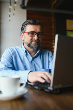 Erkek serbest yazar yeni bir iş projesi için bir kafede çalışıyor. Masadaki büyük bir pencerede oturuyor. Bir fincan kahveyle dizüstü bilgisayara bakıyor..