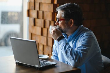 Kafede dizüstü bilgisayarda çalışan son sınıf erkek serbest yazar. uzak çalışma konsepti