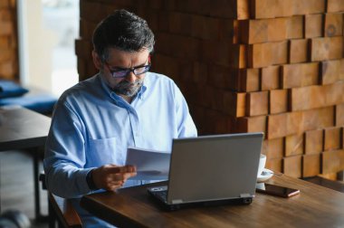 Kafede kahve içen olgun bir iş adamı. Güzel gözlükler takan, dizüstü bilgisayar kullanan, kameraya bakıp gülümseyen yakışıklı bir adamın portresi. Kahve molası.