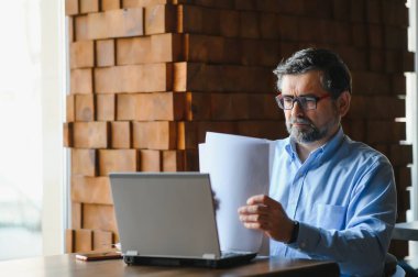 İş, teknoloji ve insan kavramı, dizüstü bilgisayarlı kıdemli işadamı modern kafede kahve içiyor.