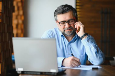 Kafede kahve içen olgun bir iş adamı. Güzel gözlükler takan, dizüstü bilgisayar kullanan, kameraya bakıp gülümseyen yakışıklı bir adamın portresi. Kahve molası.
