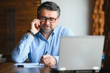 Erkek serbest yazar yeni bir iş projesi için bir kafede çalışıyor. Masadaki büyük bir pencerede oturuyor. Bir fincan kahveyle dizüstü bilgisayara bakıyor..