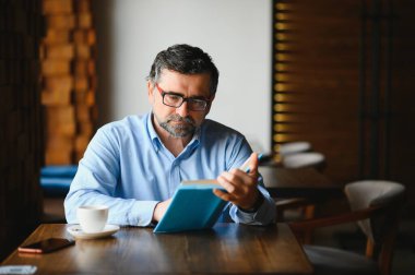 Kafede kitap okuyan olgun, yakışıklı bir adam..