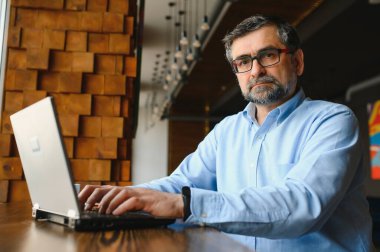 Erkek serbest yazar yeni bir iş projesi için bir kafede çalışıyor. Masadaki büyük bir pencerede oturuyor. Bir fincan kahveyle dizüstü bilgisayara bakıyor..